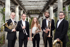 Elysium Brass Quintet standing outside with their instuments in a columned corridor