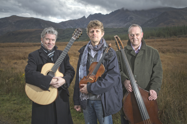 Tim Kliphuis Trio standing with their instruments in front of a range of hills