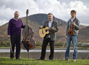 The Tim Kliphuis Trio standing with their instruments in front of a loch with a mountain in the background