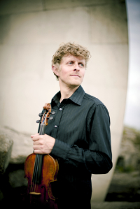 Tim Kliphuis standing, holding his violin from the neck.