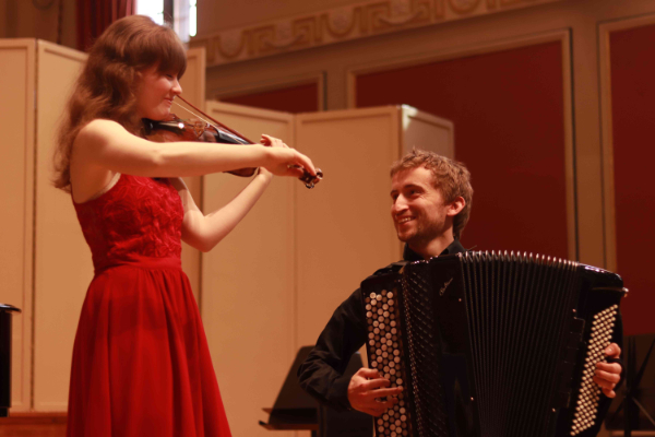 Chloë Meade standing whilst playing a violin alongside Ben de Souza sitting while playing the classical accordion