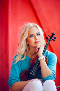 Irina Knauer sitting in front of a red background with her violin.